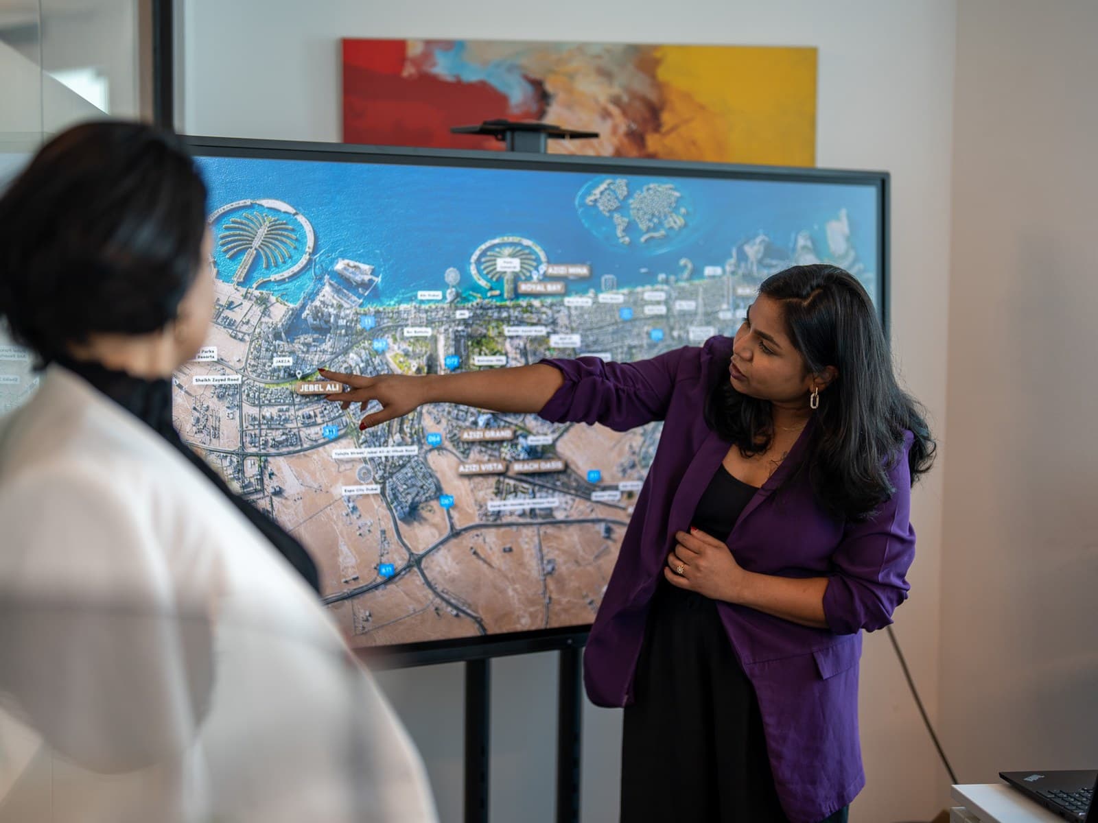 Two colleagues at a screen, one pointing out a location on a map of Dubai